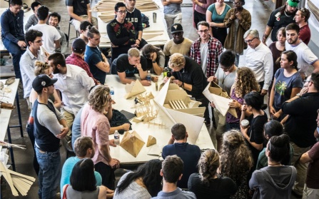Students and professors crowd around a table looking at a rough prototype for a boat. 