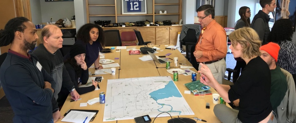 A group of urban planning faculty and students and community members from Buffalo stand over a map discussing climate resilience strategies. 