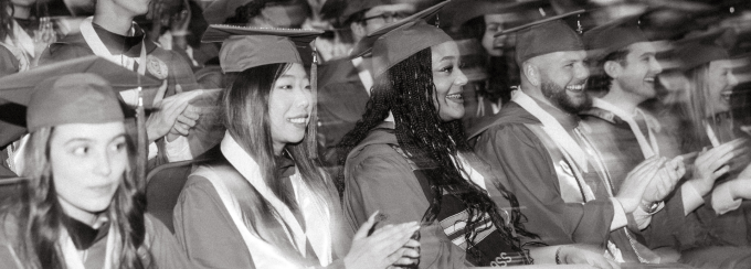 The photograph captures a group of graduates seated during the ceremony, shown in a gray-toned filter. 