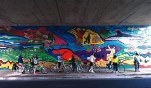 Cyclists riding under and underpass and looking at a mural. 