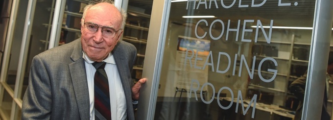 Photograph of former Dean Harold L. Cohen next to the sign for the Reading Room he sponsored. 