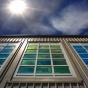 a vertical view up of a building with tinted windows and the sun shining down. 