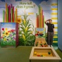 Boy stands in front of a wall labeled "How Tall Does It Grow," measuring himself against the height of different plants. 