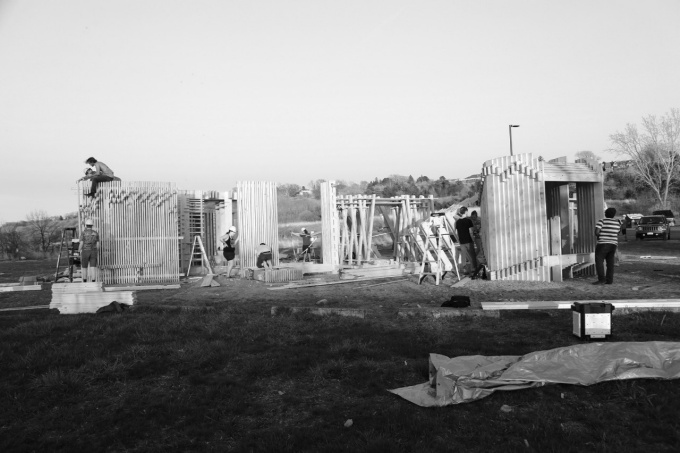 Students in hardhats climbing and working on wood structures outdoors. 